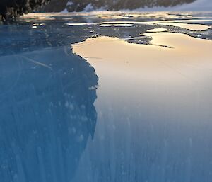 The mirrored surface of frozen lake ice reflecting back the rocky cliffs that tower above it.