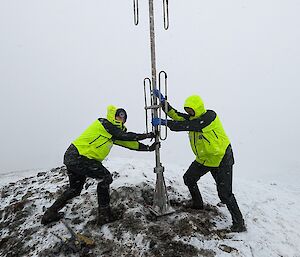 Two expeditioners holding an antenna on a snowy peak