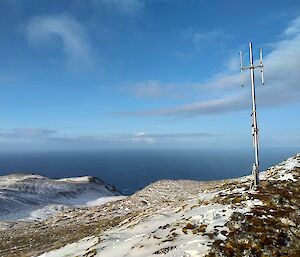 Antenna on top of a snowy peak, with ocean in the background