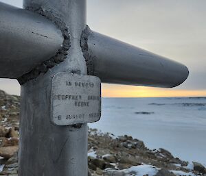 A close up photo of an engraved metal plate, welded to a steel memorial cross. The plate reads "In Memory, Geoffrey Basil Reeve, 6 August 1979"