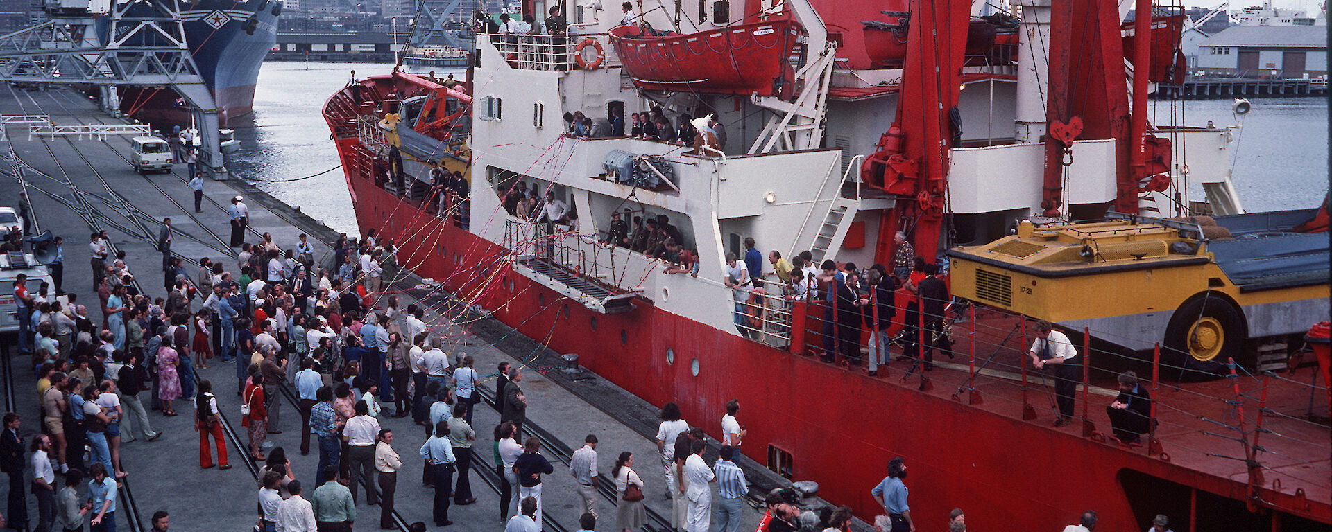 A red and white ice breaker, leaving port in front of a crowd of people