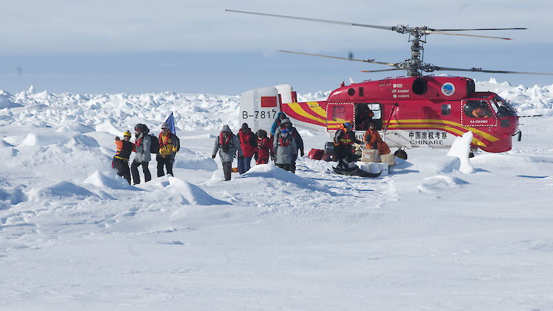 A group of people on sea ice beside a red CHINARE helicopter