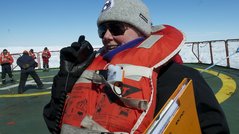 A woman wearing a life vest on the deck of a ship, with other people in life vests behind.