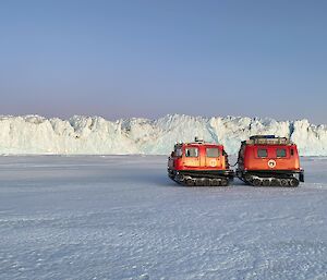 A red Hägglunds on the sea-ice with the walls of a glacier in the background.