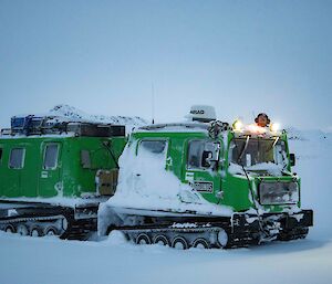A green snow vehicle with front and rear cabins sits in a snowy landscape.
