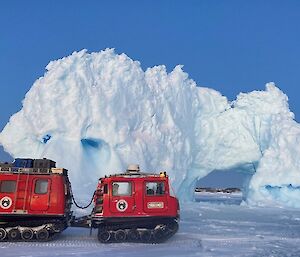 A large iceberg towers above a red snow vehicle (Hägglunds) that sits on the sea-ice