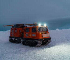 A red snow vehicle (Hägglunds) sits on the snow-covered sea-ice with grey skies in the background.