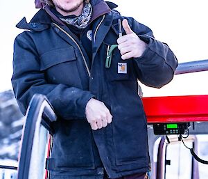 A smiling man giving a thumbs up stands in the doorway of a red Hägglunds.