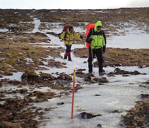 Two expeditioners walking over icy sections of a track