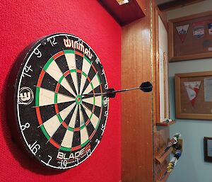 A dart is stuck into the back of another dart on a dartbord near to the bullseye.
