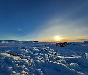 A glacier is on the left of frame stretching into the distance. Close to the camera is rubble ice formations and a Hägglunds vehicle is parked in the mid-distance on the sea ice.