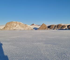 In the distance, over sea-ice, are rocky peaks rising from the shore.