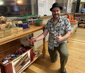 A smiling man kneeling next to a large wooden box containing a large quantity of assorted chocolate bars