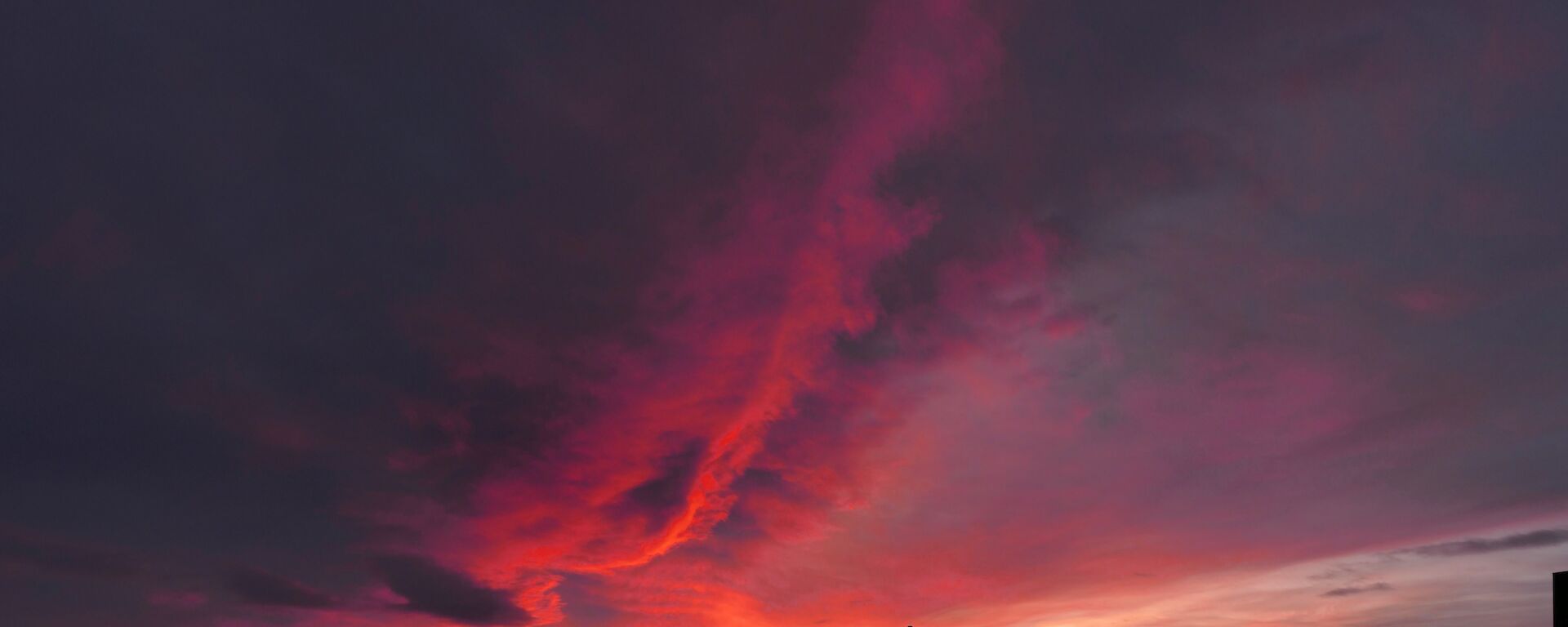 A brilliant red and purple sunset as the sun sets behind some buildings.