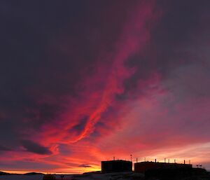 A brilliant red and purple sunset as the sun sets behind some buildings.