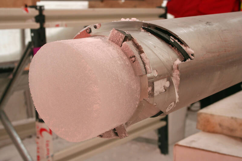 One end of an ice core protruding from a steel drill barrel.