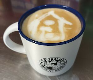 A cup of coffee with a picture of a house drawn in white milk foam on the top of it.