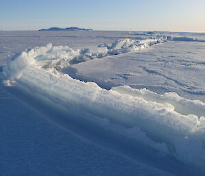 A crack in the sea ice extends into the distance. Ice is built up on the left side of the crack.