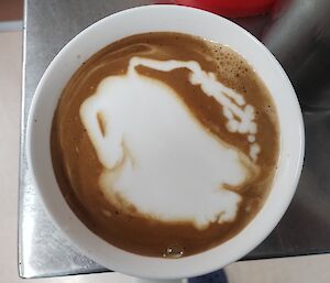 A cup of coffee with a patterned milk froth is in close focus.