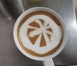 A cup of coffee with a patterned milk froth is in close focus.