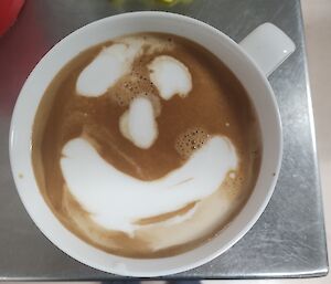 A cup of coffee with a patterned milk froth is in close focus.