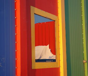 A brightly coloured blue, red, yellow and green metal-clad building with a highly reflective window is in close focus.