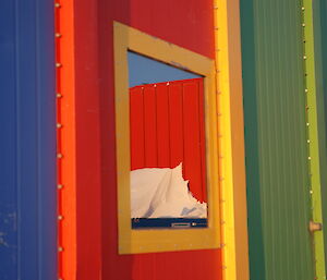 A brightly coloured blue, red, yellow and green metal-clad building with a highly reflective window is in close focus.