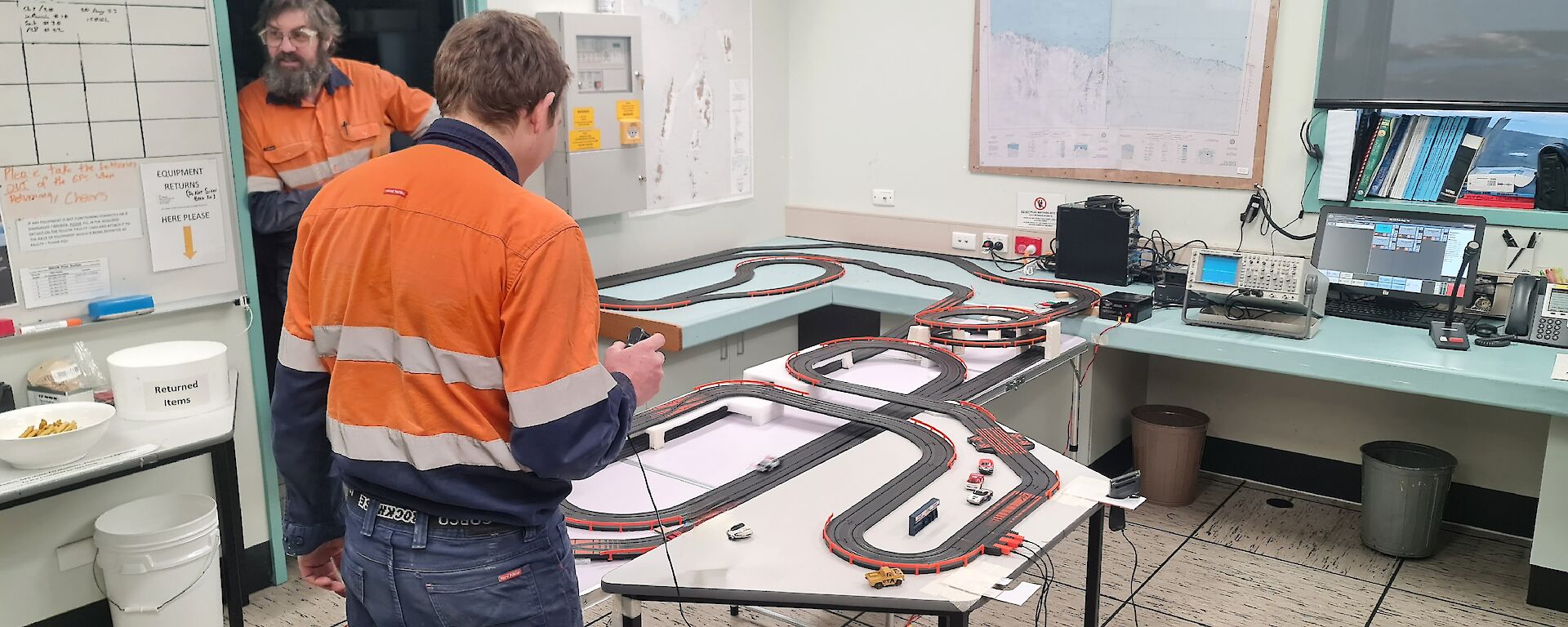 A man is controlling a toy electric race car track in an office.