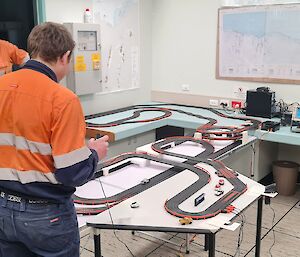 A man is controlling a toy electric race car track in an office.