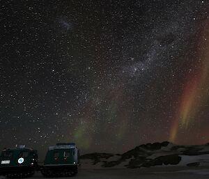 A bright orange, red and green aurora is visible with the milky way in the background. There is a Hägglunds vehicle parked to the lower left of frame.