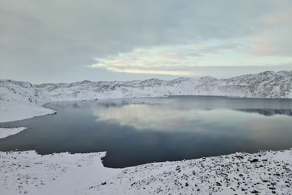 Ice forming on a lake surface surrounded by snow covered hills