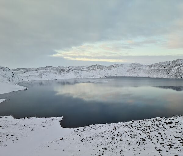 Ice forming on a lake surface surrounded by snow covered hills