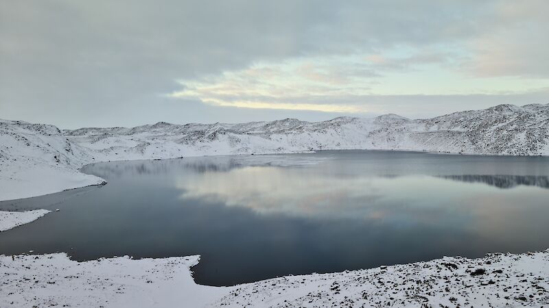 Ice forming on a lake surface surrounded by snow covered hills