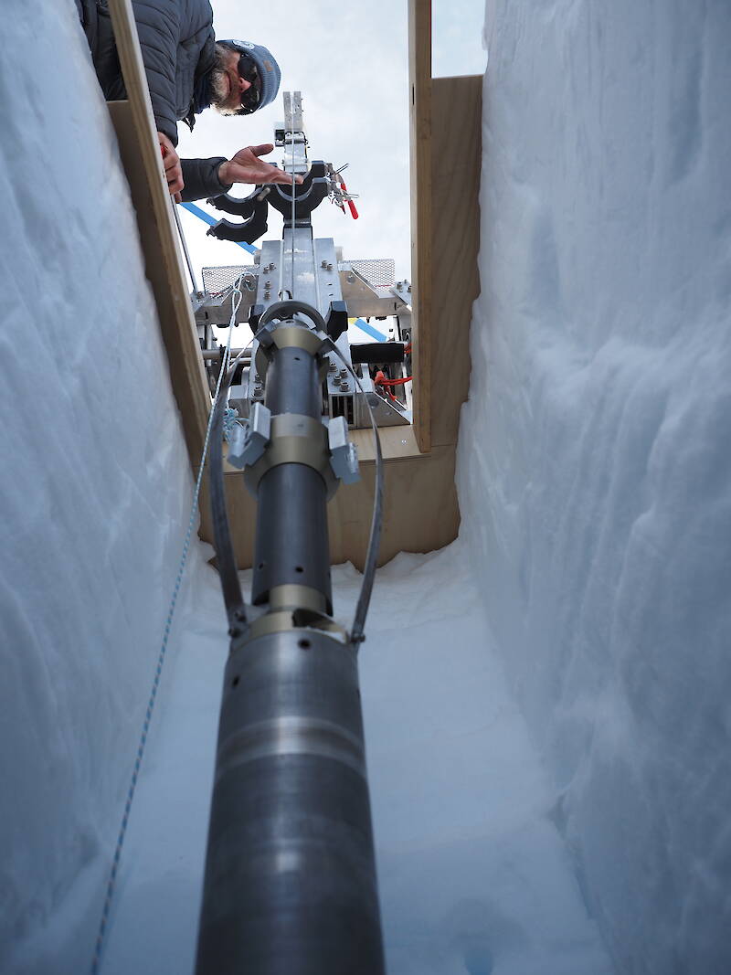 Man working with ice core drilling equipment in a hole in the ice