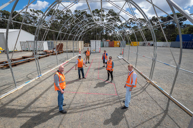 Six people stand inside the frame of a large cylindrical tent.