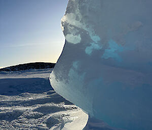 A large block of blue ice, rounded by the wind, sits with the sun shining through it.