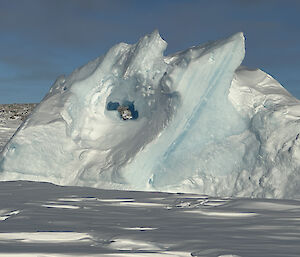 A large iceberg, tilted on an angle and trapped in the sea ice. It has a hole through the middle.