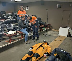 Three men standing around camera equipment filming a man lying on the ground.
