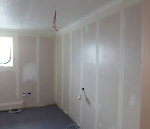 A room is being prepared for painting with walls and ceiling sanded back and seams sealed.