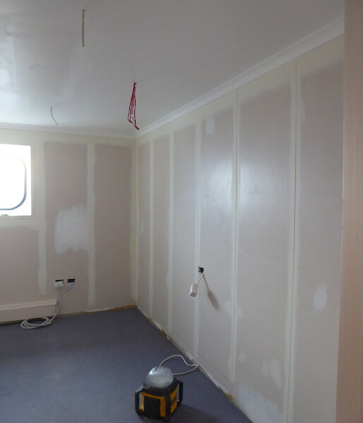 A room is being prepared for painting with walls and ceiling sanded back and seams sealed.