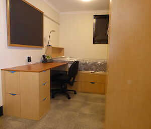 A fully renovated bedroom, with new carpet, desk, chair, and bed with mattress still wrapped in plastic.