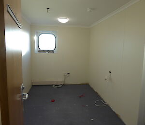 A room is being renovated with walls freshly painted white and electrical work in the midst of completion.
