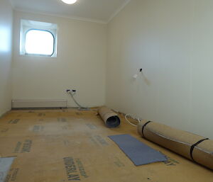 A room is in the midst of renvoation with rolled carpet and bare underlay visible. The walls of the room are freshly painted white.