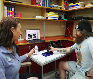 Two people sitting at a desk, examining a small medical device and output from the device on a laptop.