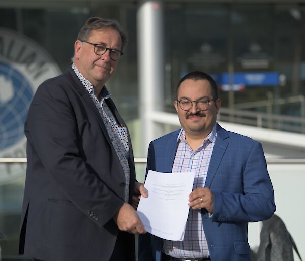 Two men standing outside a building and holding a piece of paper