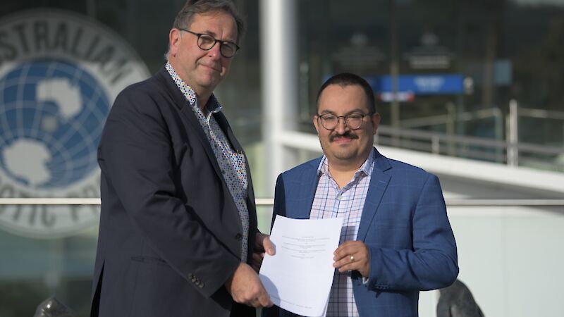 Two men standing outside a building and holding a piece of paper