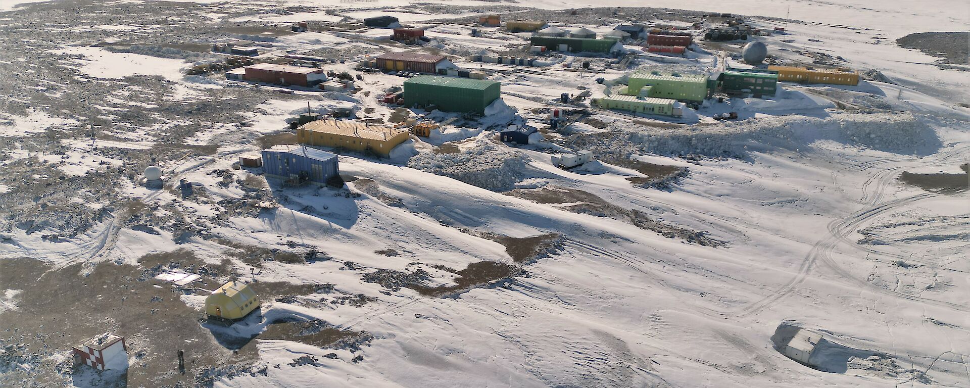Aerial shot of Davis Station showing numerous coloured buildings set into a snowy and rocky landscape.