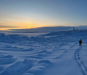 A person walks aways from camera leaving fresh footprints in the snow under a moody sky