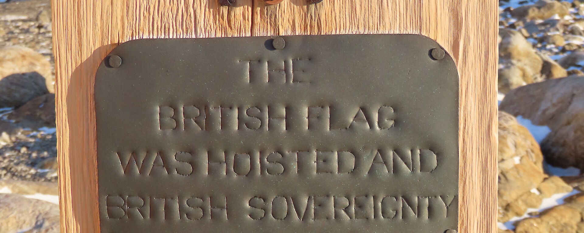 A small figurine is on top of a wooden board with a plaque proclaiming sovereignty. In the background is a rocky, snow and ice covereed landscape.