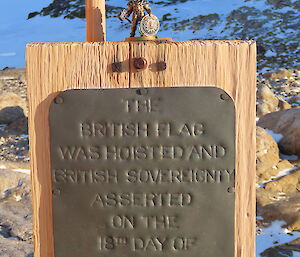 A small figurine is on top of a wooden board with a plaque proclaiming sovereignty. In the background is a rocky, snow and ice covereed landscape.